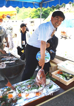 가카라시마 주민이 제공한 커다란 생선 입 속에 손가락을 넣고 익살스런 표정을 짓는 이준원 시장